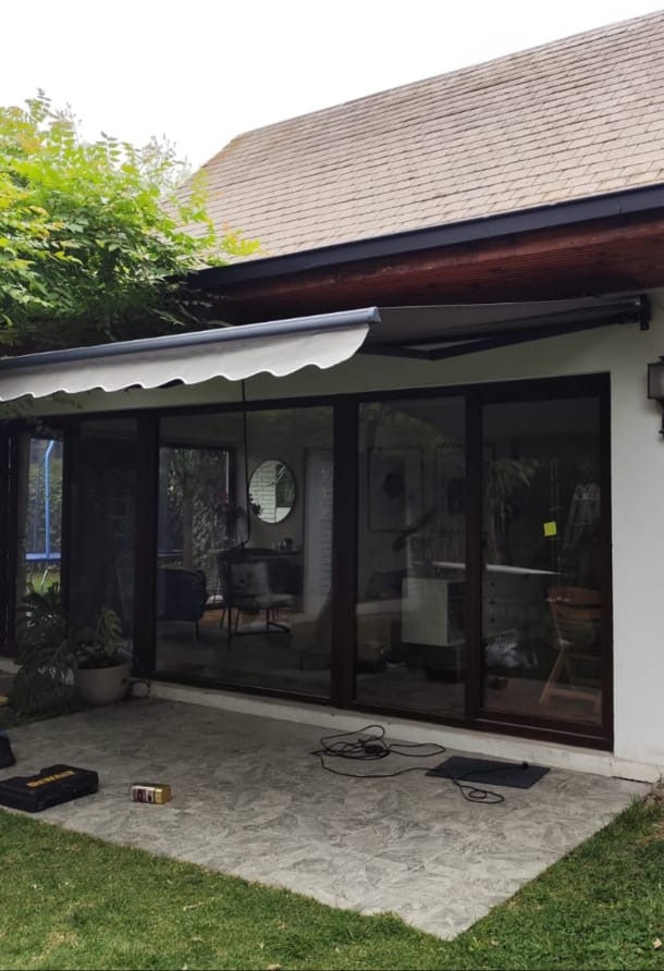Toldo retráctil gris instalado sobre una terraza, visto desde el patio